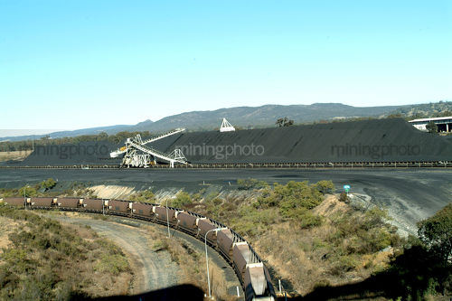 Coal train being loaded at coal mine site with reclaimer and coal stockpiles in background. - Mining Photo Stock Library