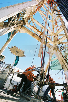 Workers on an oil gas rig in the desert fixing pipe in the hole. - Mining Photo Stock Library