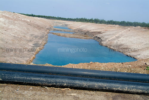 Half full dam with black water pipe in foreground - Mining Photo Stock Library