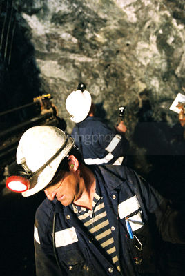 Male underground worker with other worker inspecting roof and excavations in background. - Mining Photo Stock Library