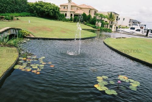 Exclusive marina residential living with water feature and moored boat next to house in background - Mining Photo Stock Library