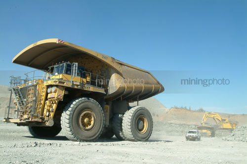 Coal haul trucks leaving opencut mine floor after being loaded by digger with light vehicle behind - Mining Photo Stock Library