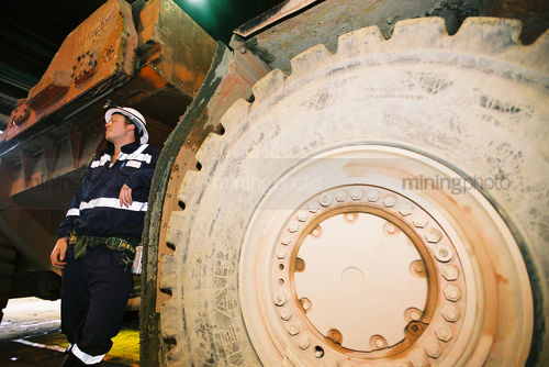 Underground mine worker standing next to wheel of machinery - Mining Photo Stock Library