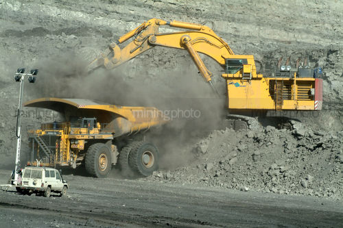 Digger loading coal haul truck in a cloud of dust with light vehicle in foreground - Mining Photo Stock Library