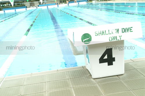 Starting block at public swimming pool with marked lane going to the distance - Mining Photo Stock Library