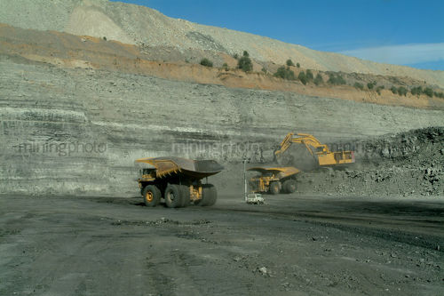 Truck rotation on haul road with digger loading and light vehicle in foreground. opencut high walls behind - Mining Photo Stock Library