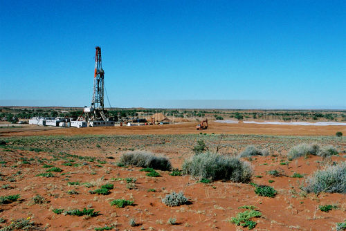 Oil and gas drill rig in the desert.  shot from a distance to show soil,  vegetation and harsh environment. - Mining Photo Stock Library