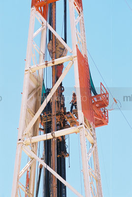 Drill rig worker high up the derrick loading pipe into the hole - Mining Photo Stock Library