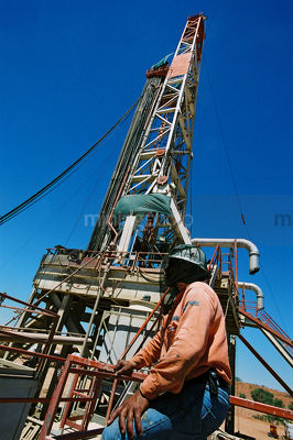 Drill rig worker  with fly net  over his head onsite with derrick in background. - Mining Photo Stock Library