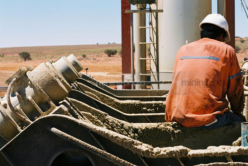 Drill rig worker taking a few minutes to rest on the derrick.  shot from behind. - Mining Photo Stock Library