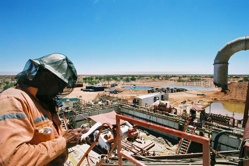 Drill rig worker witha  fly net over his head taking notes around the rig site. - Mining Photo Stock Library
