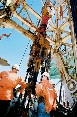 Drill rig workers standing on the platform with the derrick above.  shot from behind - Mining Photo Stock Library