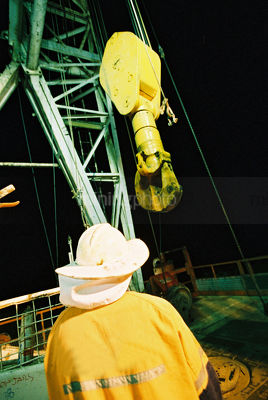 Oil and gas rig worker next to derrick hook. shot from behind - Mining Photo Stock Library