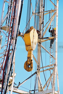 Oil and gas rig worker climbing up the derrick with safety harness on.  derrick hook in the foreground. - Mining Photo Stock Library