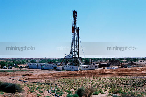 Drill rig in the desert with vegetation and sandy soil in foreground - Mining Photo Stock Library