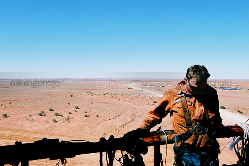 Drill rig worker on top of derrick with australian desert in background - Mining Photo Stock Library