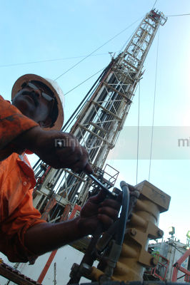 Drill rig worker tightening bolt with spanner looking into distance with derrick behind. - Mining Photo Stock Library
