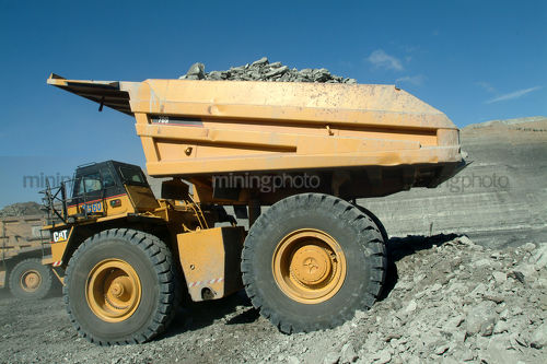 Coal truck emptying overburden onto stockpile with high walls behind - Mining Photo Stock Library