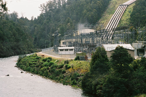 Hydro power plant with water pipes leading back up the hill.  plant is on a river. - Mining Photo Stock Library