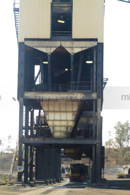 Large hopper delivering ore product to trucks underneath - Mining Photo Stock Library
