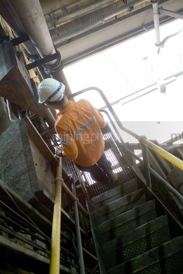 Mine worker walking down steps inside a processing plant. shot from behind. - Mining Photo Stock Library
