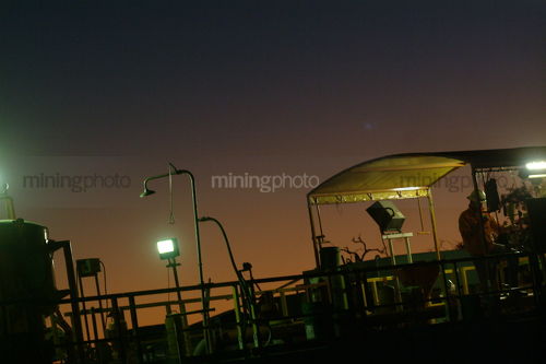 Workers on drill rig working under lights at dusk. - Mining Photo Stock Library