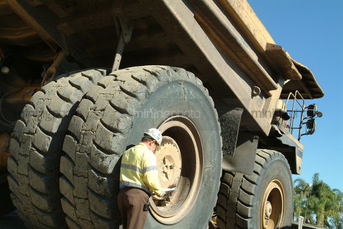 Mine site supervisor standing against huge haul truck tyre. shot from behind. - Mining Photo Stock Library