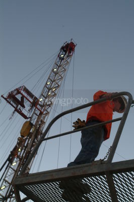 Drill rig worker standing on steel walkway with derrick behind.  shot from below. - Mining Photo Stock Library