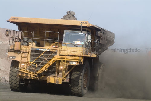 Loaded haul truck amidst a cloud of dust driving along haul road. - Mining Photo Stock Library