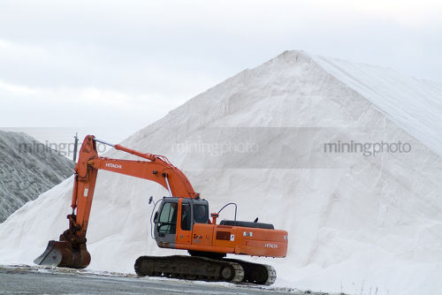 Parked excavator in front of white product stockpile.  - Mining Photo Stock Library