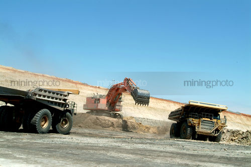 Haul truck being loaded by excavator in opencut mine site with another truck waiting close by. - Mining Photo Stock Library