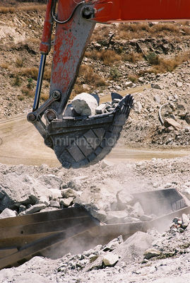 Excavator bucket loading hard metal into the back of a haul truck in open cut mine site.  shot up close. - Mining Photo Stock Library