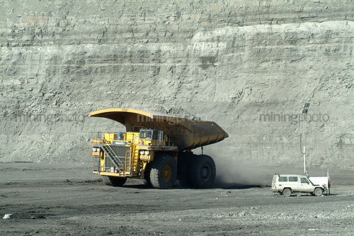 Coal haul truck driving along opencut mine site with light vehicle and high walls behind - Mining Photo Stock Library