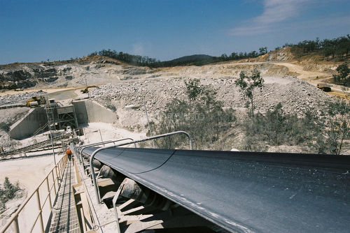 Long high conveyor with mine worker down walkway.  open cut mine site in background. - Mining Photo Stock Library