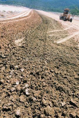Closeup of dirt on road with grader out of focus in background. - Mining Photo Stock Library