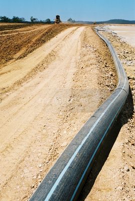 Large black water pipe on graded  road next to dam on mine site - Mining Photo Stock Library
