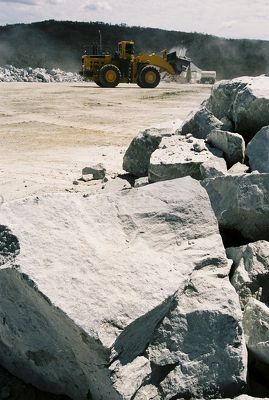 Large hard metal overburden rocks in foreground with working loader in background - Mining Photo Stock Library