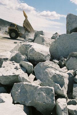 Haul truck tipping its load onto stockpile in background with hard metal rocks in foreground. - Mining Photo Stock Library