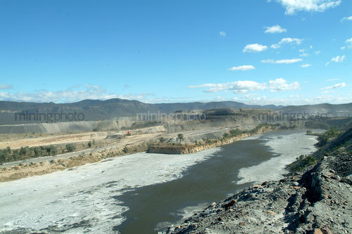 Wide shot of coal tailings dam with diggers and haul trucks working behind - Mining Photo Stock Library