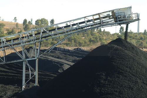 Conveyor stockpiling coal with power station smokestack in distance  - Mining Photo Stock Library