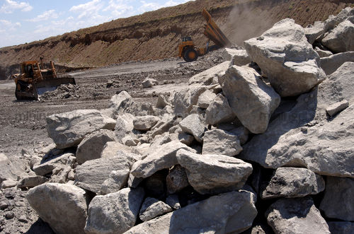 Haul truck dumps overburden at stockpile site of hard metal open cut mine.  rocks in foreground - Mining Photo Stock Library