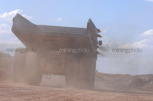 Dusty shot from behind of haul truck traveling along haul road. - Mining Photo Stock Library