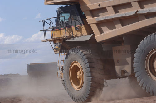 Closeup of moving haul truck turning a corner in cloud of dust - Mining Photo Stock Library