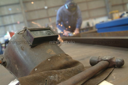 Worker grinding with lots of sparks in workshop with separate hammer and welders mask in foreground. - Mining Photo Stock Library