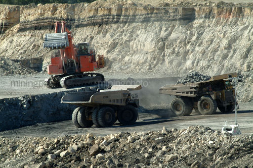 Digger loading coal haul trucks with overburden. visible coal seam behind. great truck rotation shot - Mining Photo Stock Library