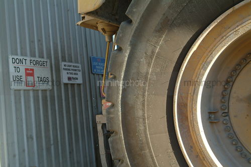 Large mine haul truck parked next to safety signs at workshop. truck shot close so only wheel and tyre is seen. - Mining Photo Stock Library