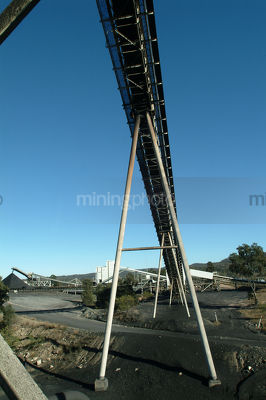 Large A frame conveyor with stockpiles of coal in background.  shot from under conveyor.  graduated blue sky behind. - Mining Photo Stock Library