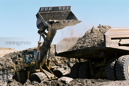 Loader loading a haul truck with overburden on open cut mine site - Mining Photo Stock Library