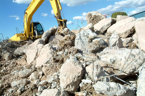 Excavator rock breaking through concrete demolition.  concrete pieces in foreground. - Mining Photo Stock Library