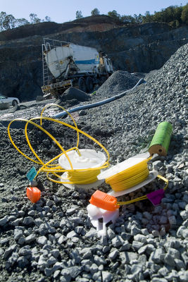 Colourful blasting equipment next to blast hole on mine site quarry.  close up at ground level with blast truck and gear in background. - Mining Photo Stock Library